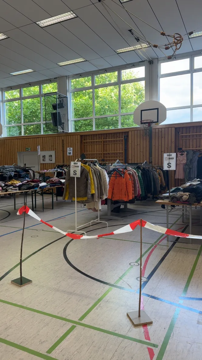 Verkaufsraum in der Turnhalle: Kleiderständer und Tische, nach Größen sortiert